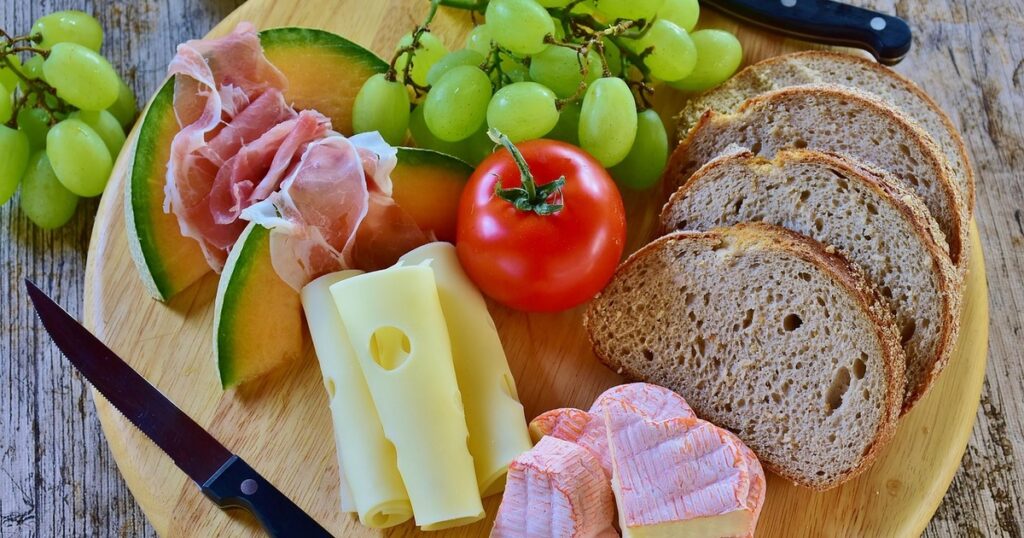 Wooden plate with cheese, sliced ham, rye bread and fruit representing sources of B vitamins